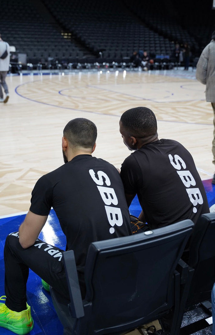 Behrad & Denzel from Simply British Ballers. (SBB.) sit down next to a basketball court in discussion 