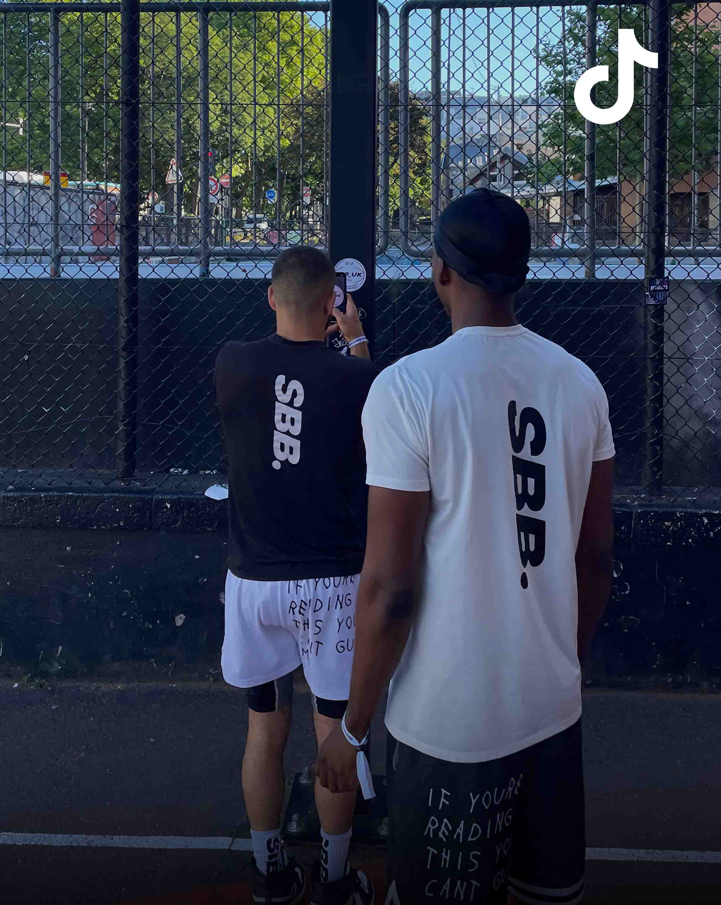 Behrad & Denzel from Simply British Ballers. (SBB.) stand on a basketball court in Balti Zone Paris putting up a signature SBB sticker on the basekt